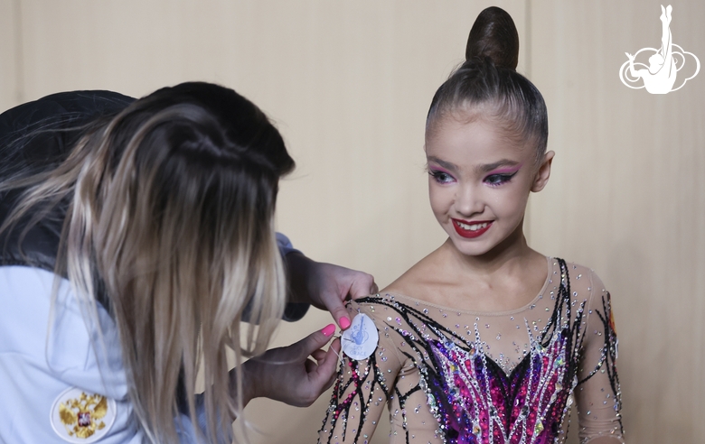 Academy coach Evgeniya Eliseeva sews on a patch with the Sky Grace-2023 tournament logo onto Ksenia Savinova’s sleeve