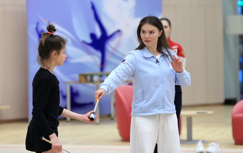 Alina Kabaeva shows the movement with the club to the young gymnast Karolina Tarasova